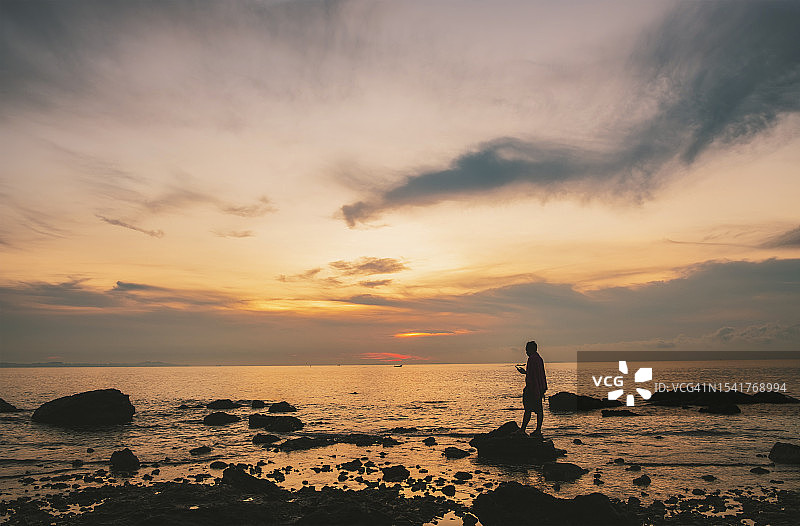 日出时，一个人站在岩石上，对着大海和天空图片素材