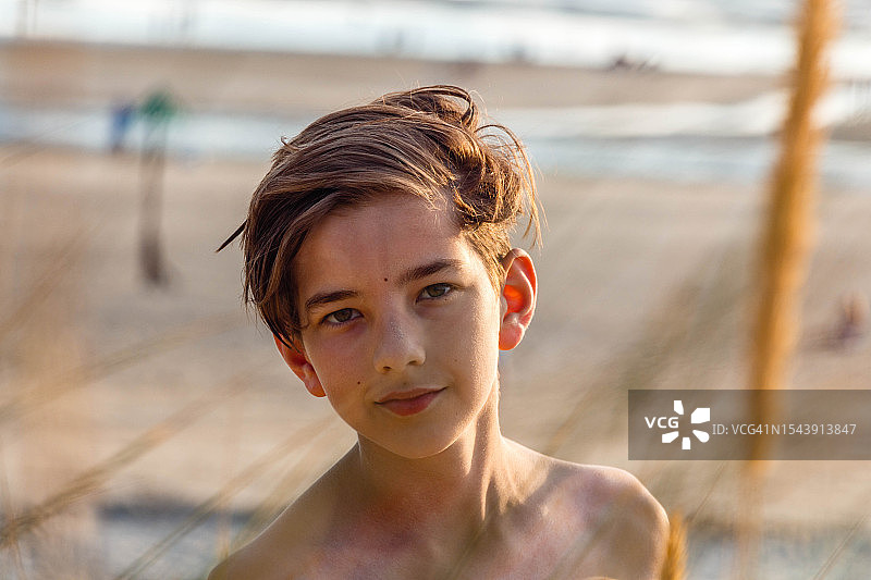 一个男孩的肖像，在黄金时间日落的沙滩海岸线上看着相机图片素材