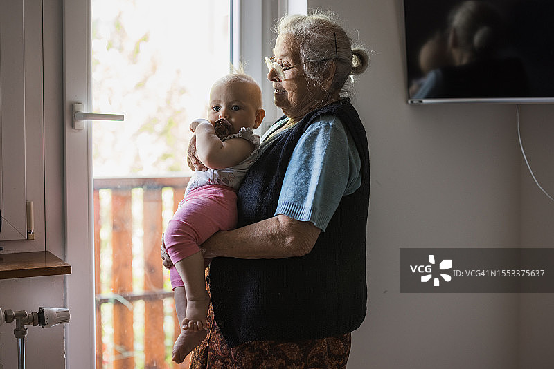 一位老年妇女抱着一个婴儿，透过窗户望着窗外图片素材