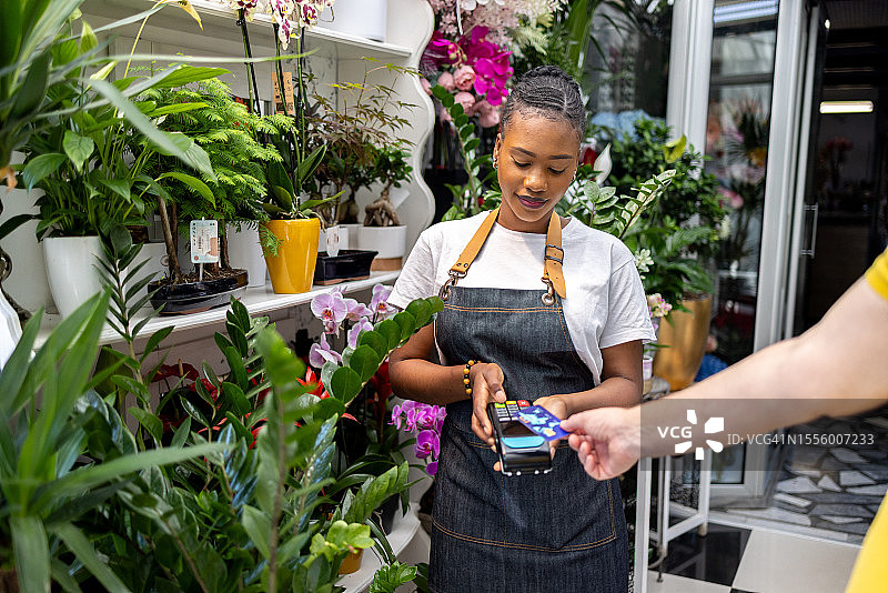 女花店黑人手持POS机，顾客用信用卡付款图片素材