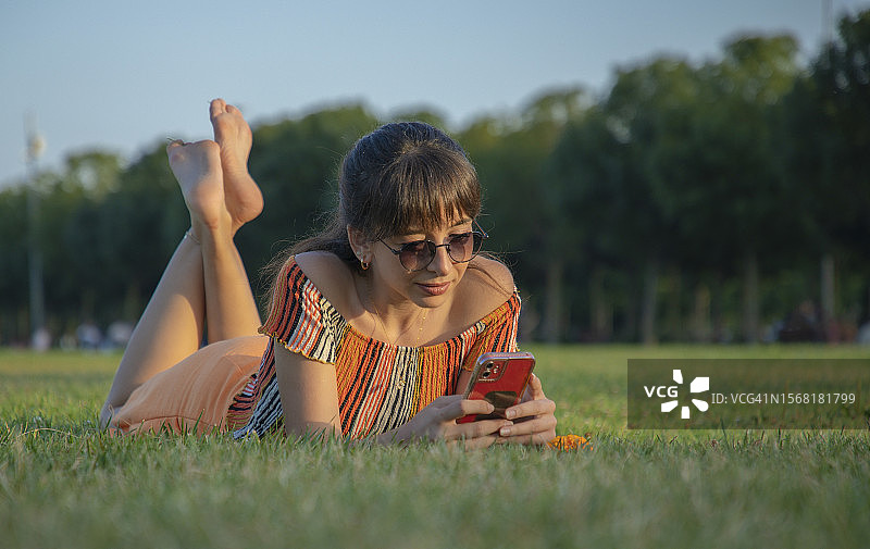 穿着艳丽的年轻女子在公园里玩手机图片素材