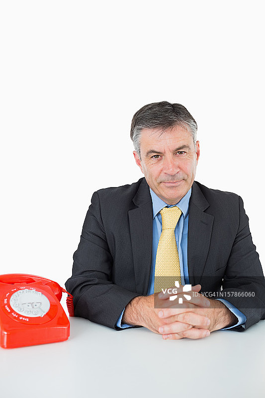 一个拿着电话坐在办公桌前的严肃男人图片素材