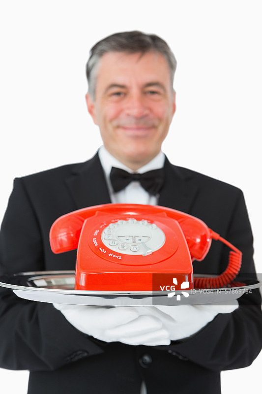 微笑的服务员拿着一个红色的电话图片素材