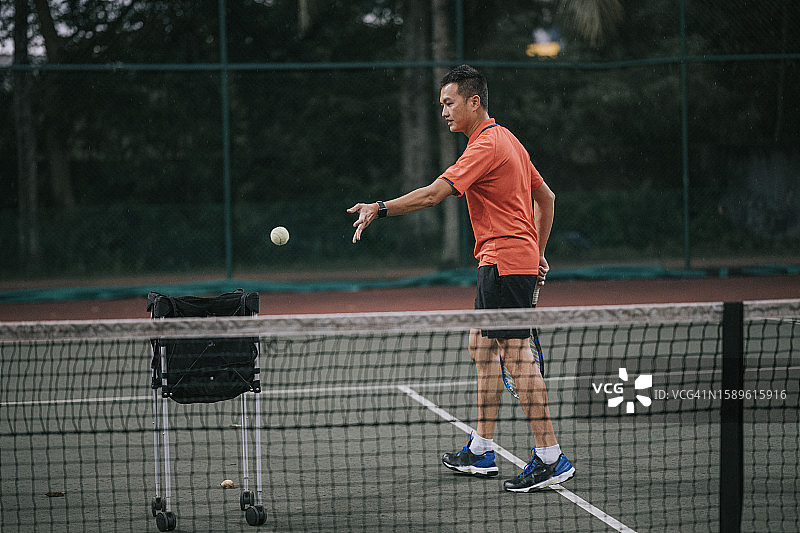 亚洲华人男子网球运动员在训练后在网球场捡网球图片素材