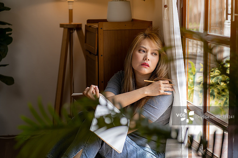 紧张、忧虑和沮丧的女人坐在房子靠窗的椅子上。图片素材