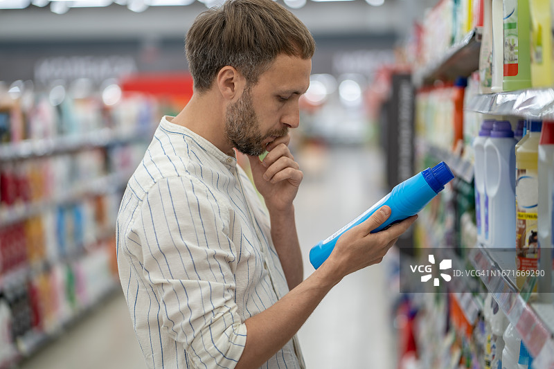 集中男子在超市购物，阅读产品信息部的家用化学品。图片素材