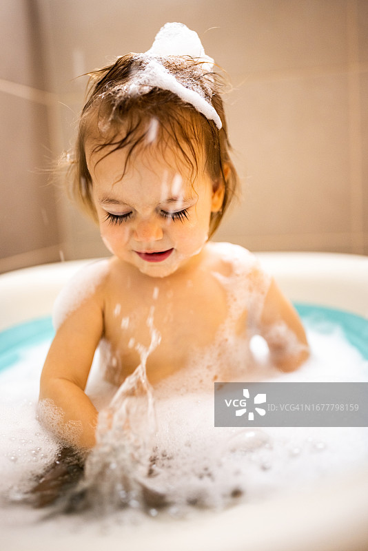 可爱的小女孩在浴缸里玩白色泡沫图片素材