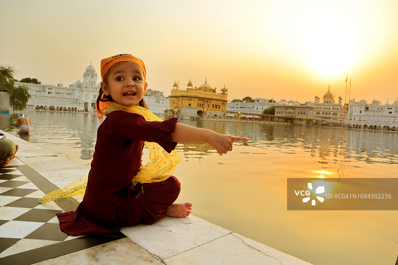 女婴坐在印度金庙的池塘旁图片素材