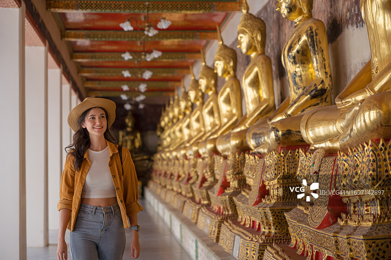 在曼谷卧佛寺，一名女游客走在一排佛像旁边。图片素材