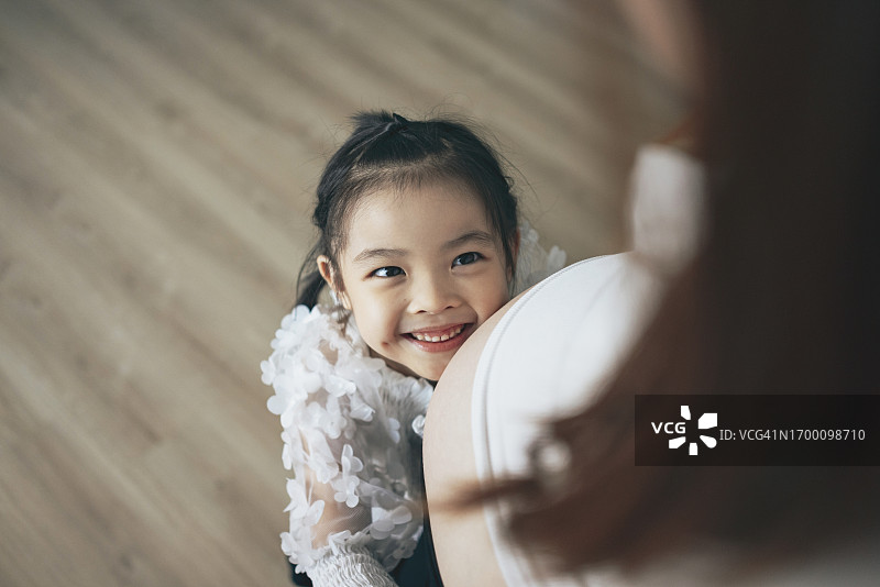 一个年轻的亚洲女孩抱着妈妈的肚子，感受着宝宝的动作和心跳，展示着家庭中的爱和关怀，以及对新成员到来的期待。图片素材