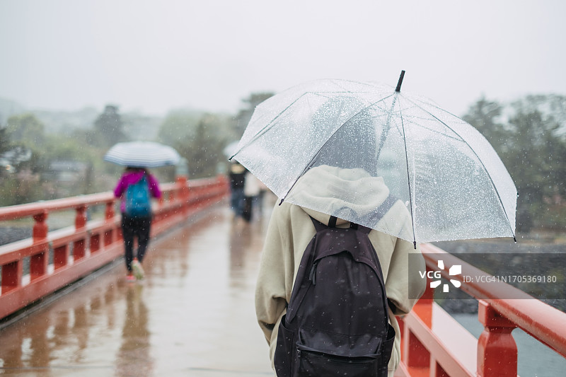 一个阴沉的日子里，孤独的年轻亚洲女子在雨中撑着伞走在宇治的人行桥上的后景。放松、旅游、休闲、度假的理念。图片素材