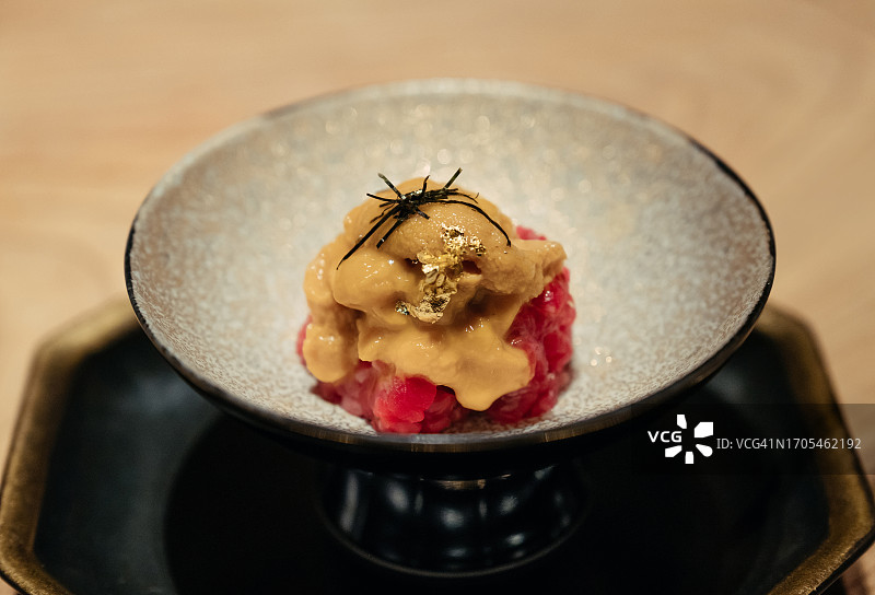日本餐馆里，餐桌上一碗新鲜的海胆和生牛肉的特写。亚洲美食和饮食文化。外出就餐的生活方式。图片素材
