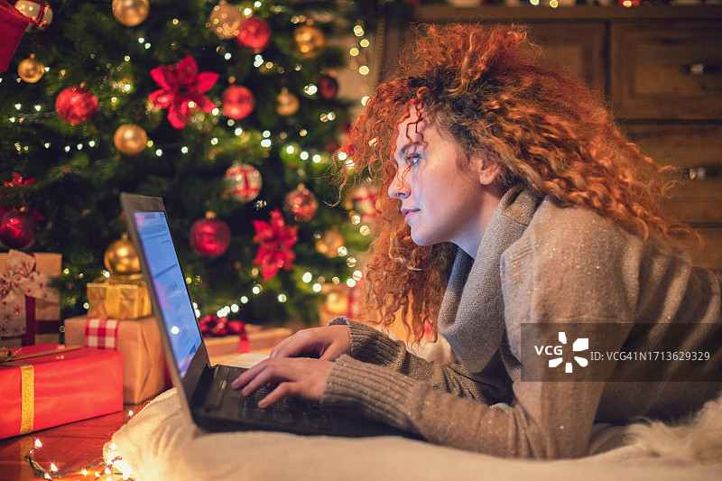 在温馨的圣诞气氛中，年轻漂亮的女人在家里使用笔记本电脑图片素材