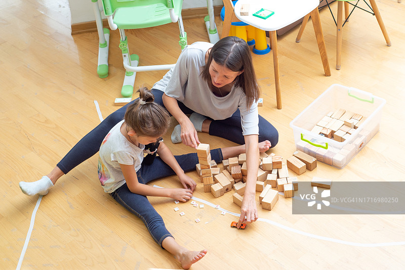 一名年轻女子在房子的地板上和一个孩子玩着木块。图片素材