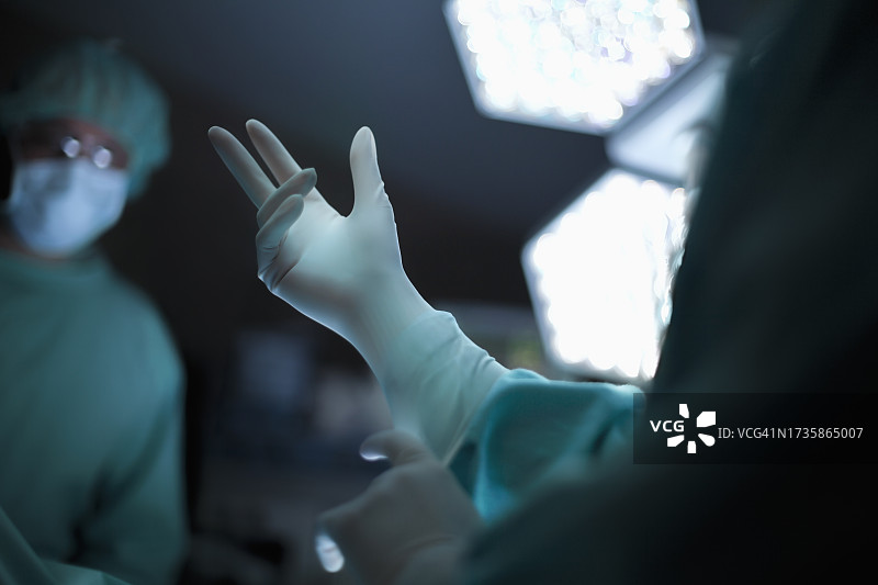 医疗专业医生护士在医院手术室准备手术，与同事一起戴上乳胶手套防护工作服，以确保安全图片素材