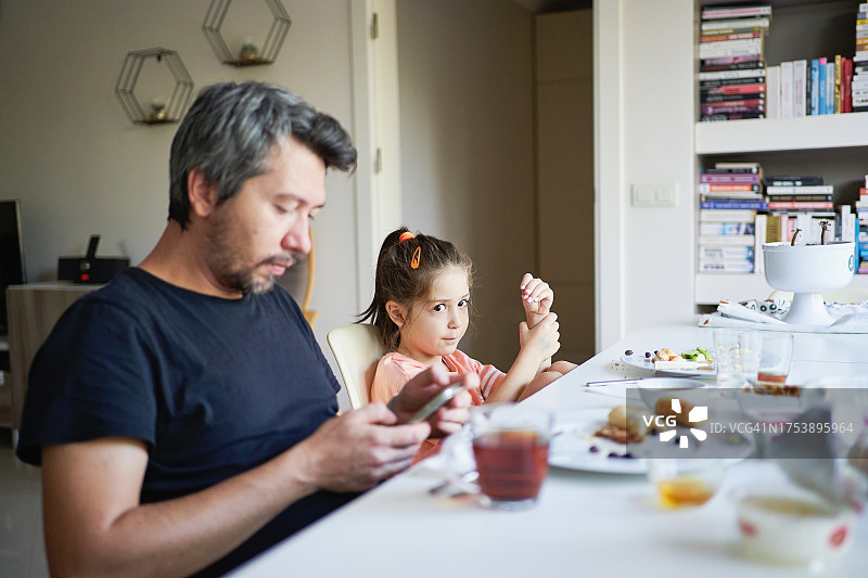 父亲和女儿在早餐时使用移动设备图片素材