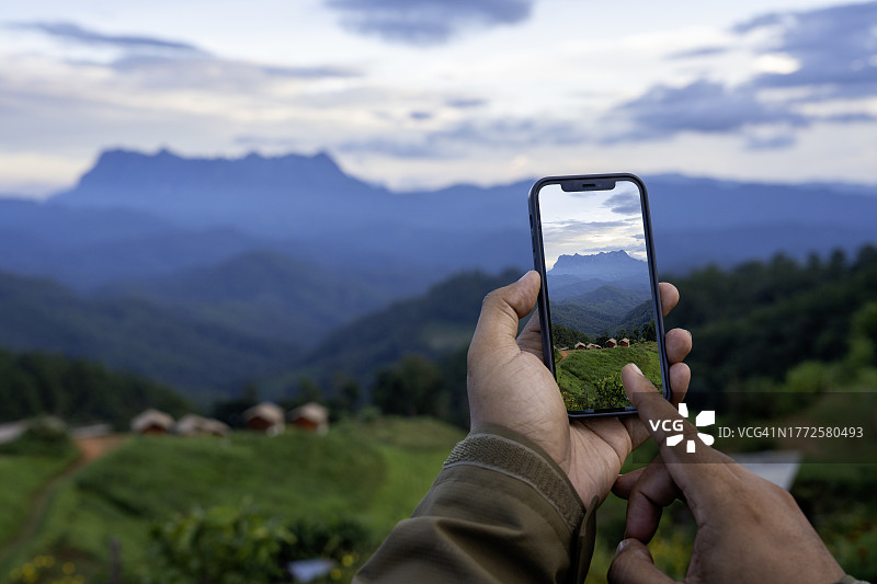 一名男子手里拿着一部智能手机，上面展示着山脉的照片。图片素材