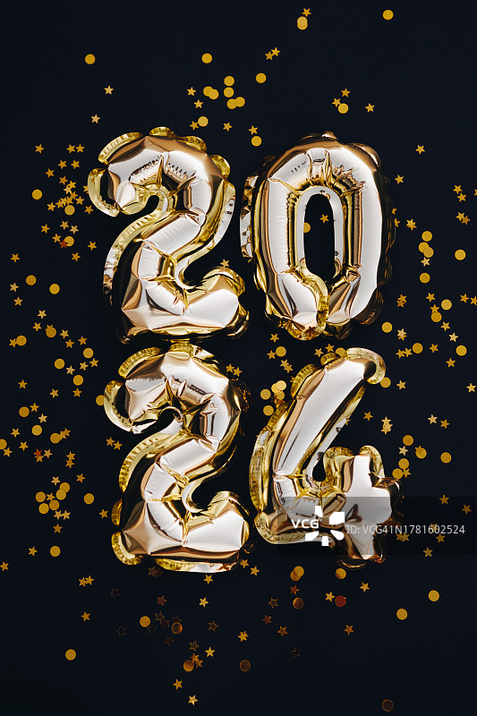 2024年新年贺卡。在黑色的背景上用金色的五彩纸屑衬托金色的气球图片素材