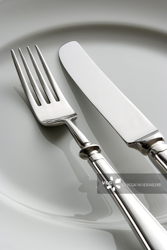 在白色盘子上的叉和刀的特写。图片素材