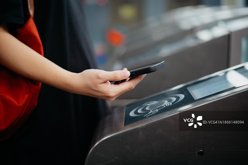 一名女子在地铁站检票，通过智能手机快速便捷地进行非接触式支付。NFC技术，点走概念。图片素材