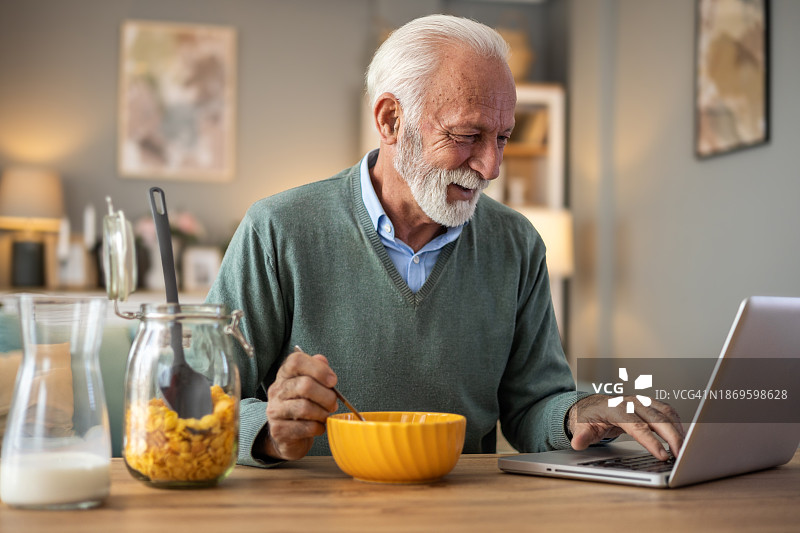 退休男子准备玉米片早餐，用笔记本电脑看新闻图片素材