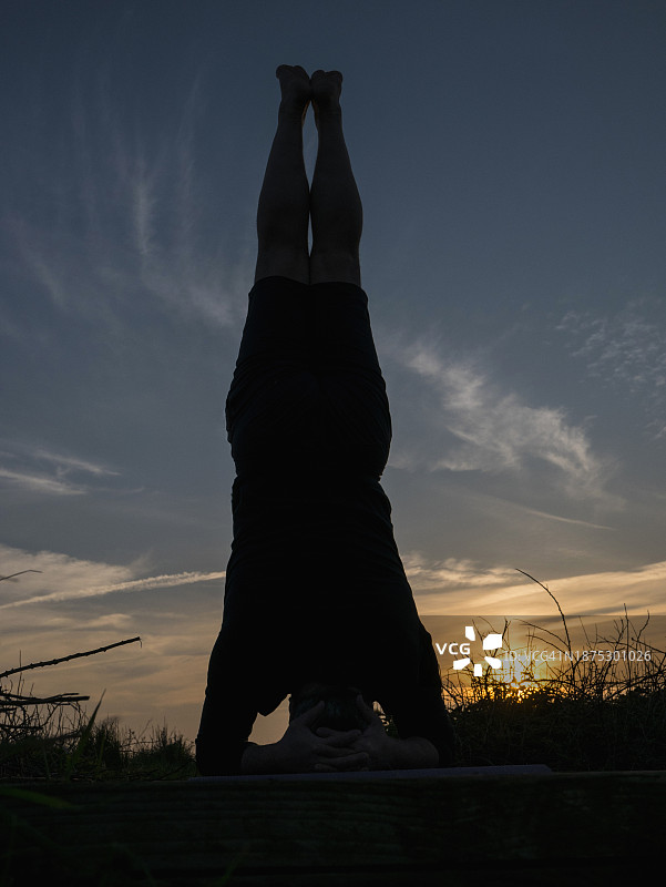 男子在日落时分在户外练习瑜伽，头倒立姿势图片素材