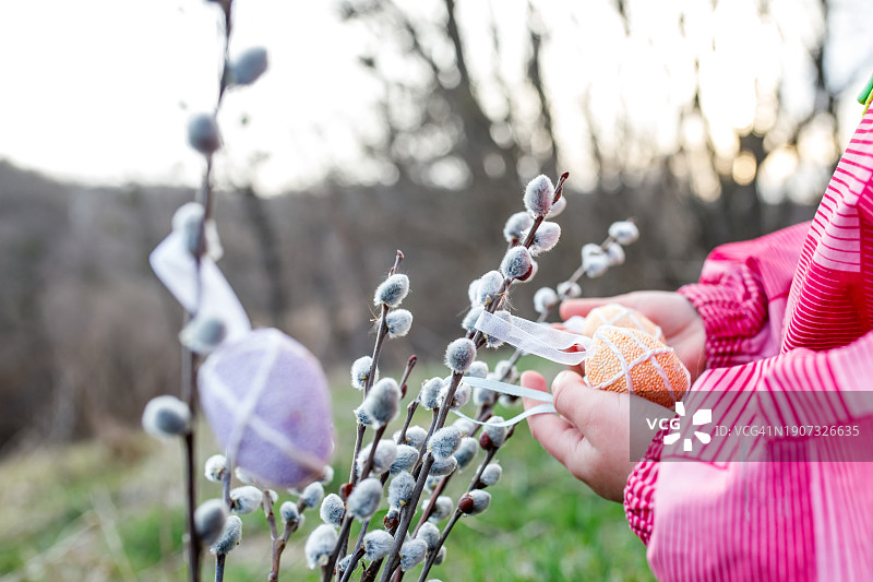 一个孩子的手在绿草地上的柳枝上挂复活节彩蛋图片素材