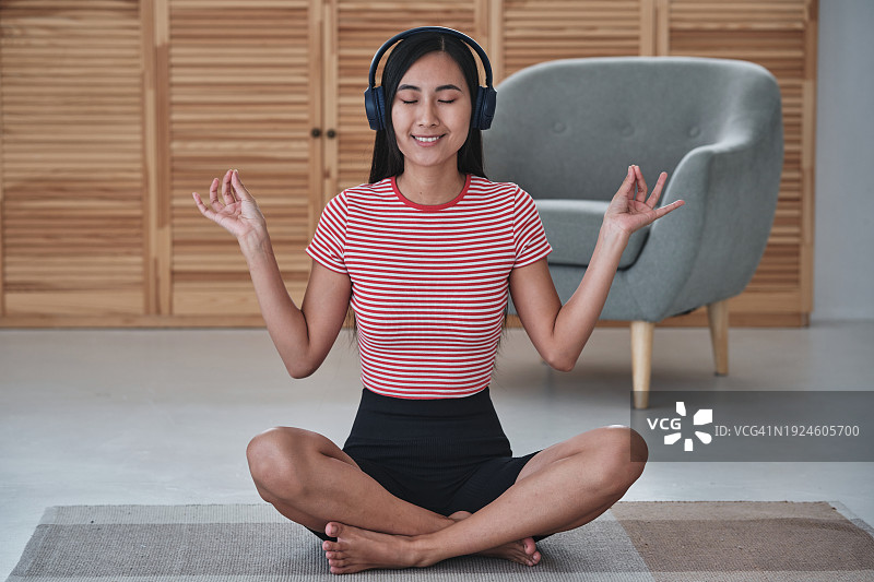 快乐健康的亚洲妇女戴着无线耳机在家冥想，在家练习瑜伽时听在线冥想图片素材
