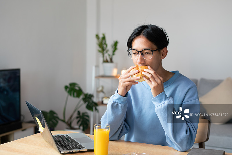 一个男人在家里用笔记本电脑工作，吃早餐和饮料。图片素材