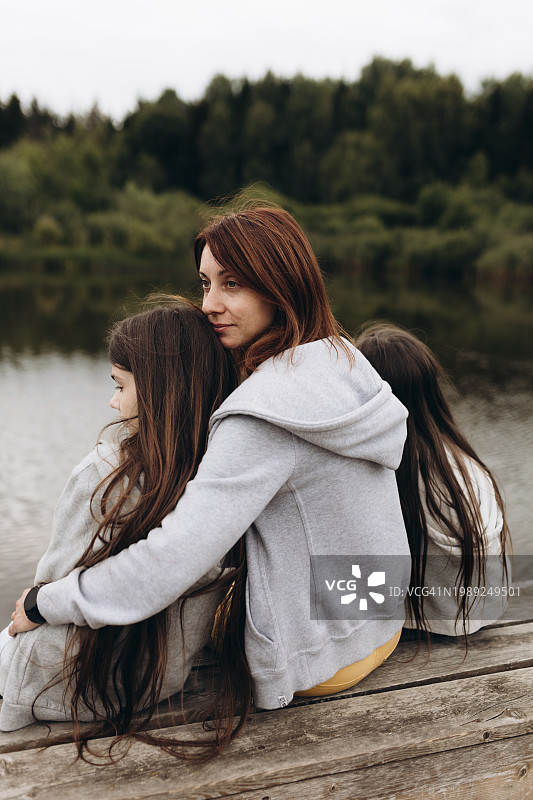 母亲和两个女孩坐在湖边的防波堤上的后景图片素材