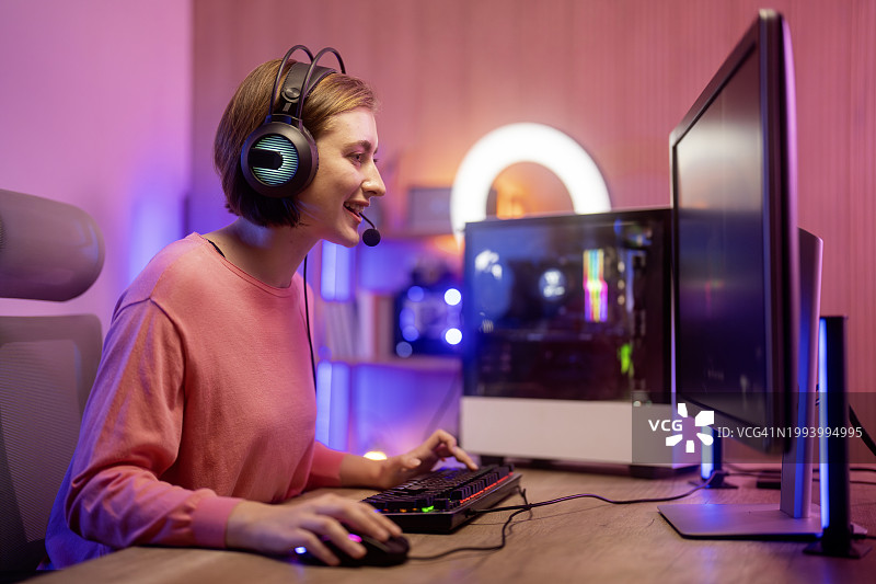 在她的电脑上玩在线视频游戏。房间和电脑有彩色霓虹灯。舒适的夜晚在家里。图片素材