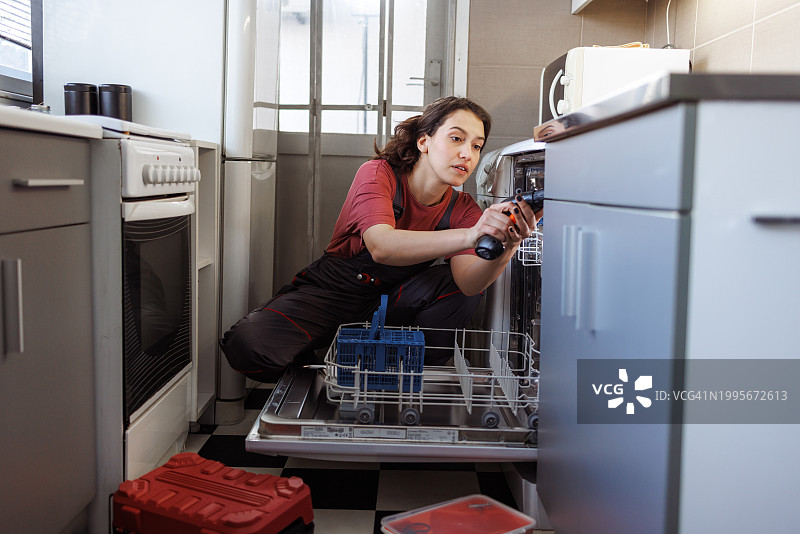 一个年轻的女人在修理洗碗机图片素材