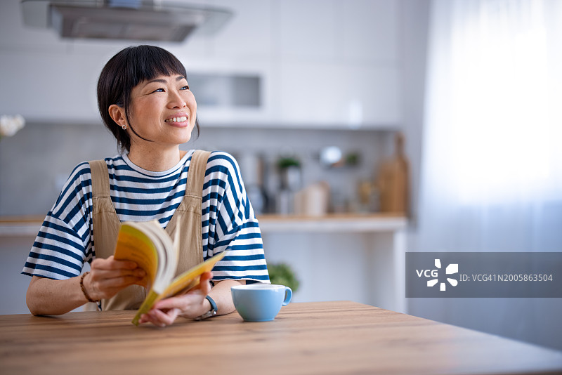亚洲女性在家里放松，看书，喝酒图片素材