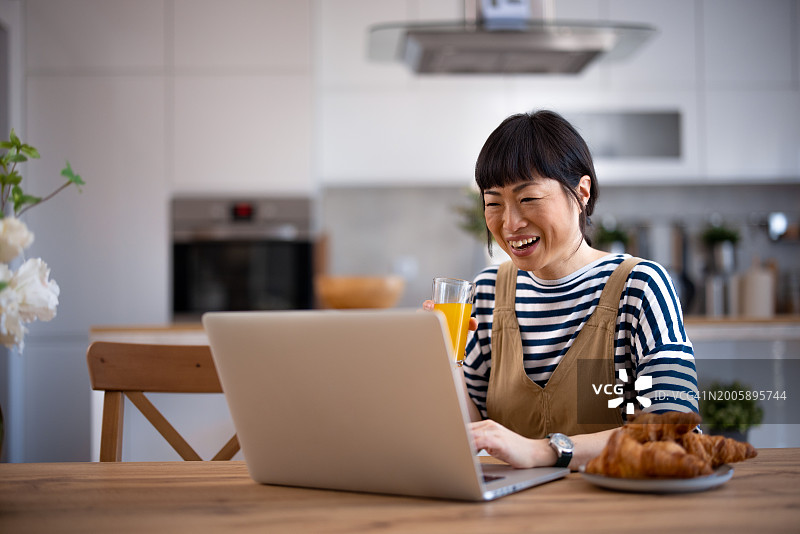 一个亚洲女人一边用笔记本电脑打字一边吃早餐图片素材