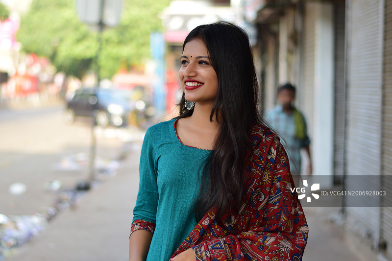 一个年轻美丽的女人站在街上，微笑着，穿着印度传统服装。图片素材