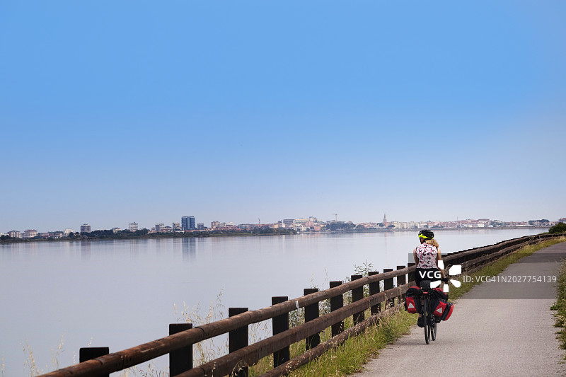 女自行车游客，穿过泻湖桥进入格拉多，意大利图片素材