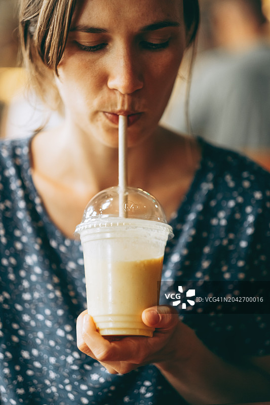 一张聚焦的照片捕捉到一个女人用吸管啜着奶油水果奶昔，闭着眼睛享受着简单的快乐。图片素材