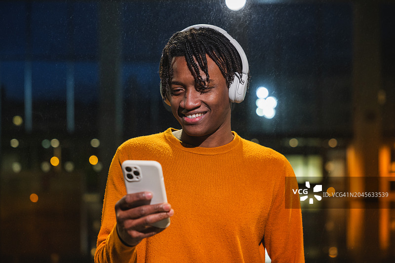 年轻的非裔美国人戴着白色耳机听音乐，沉浸在数字世界中。图片素材
