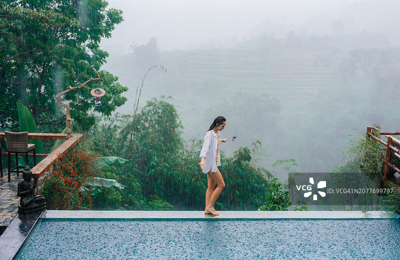 雨中，女子在巴厘岛别墅的泳池边放松图片素材
