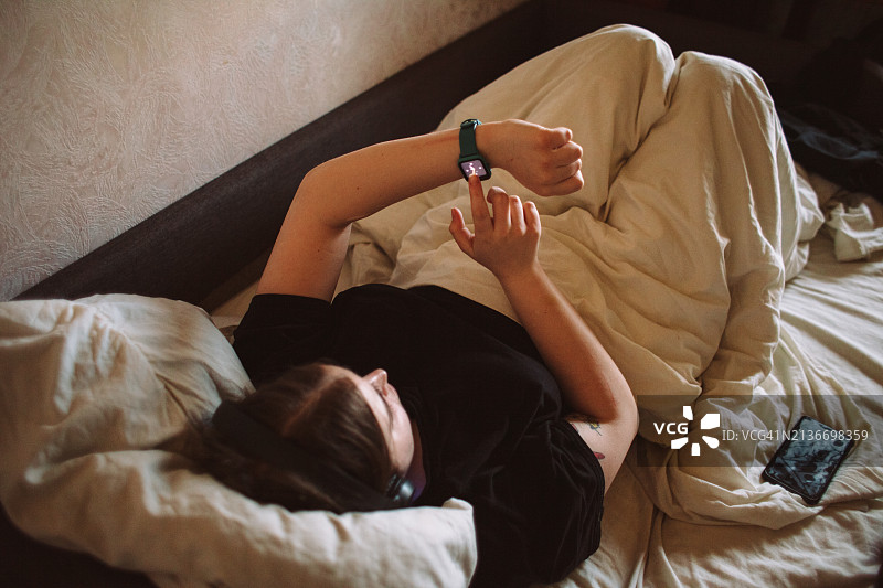 年轻女子躺在床上使用智能手表图片素材