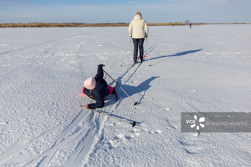 女孩在雪地里追妈妈滑雪时摔倒了。图片素材