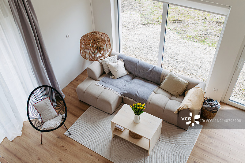时尚的客厅内部配有沙发，装饰简单的木制咖啡桌，硬木地板上的地毯。大全景窗。图片素材