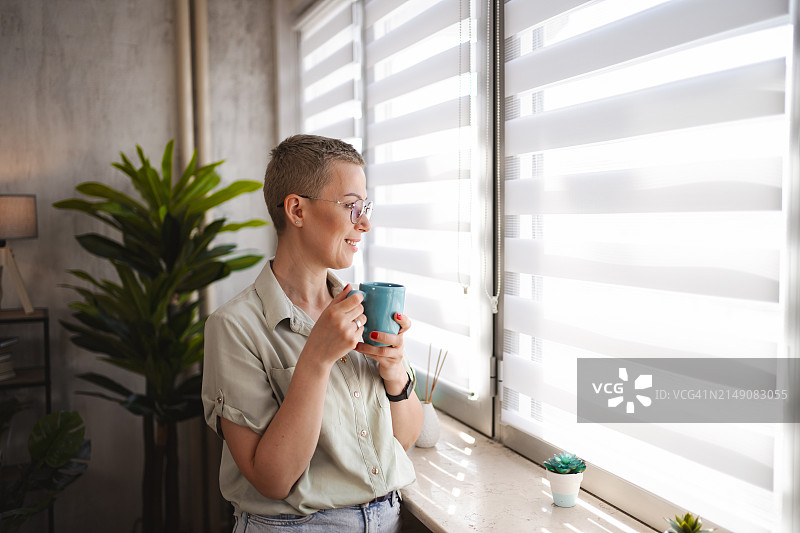 一个短头发的女人一边喝咖啡，一边从公寓里往窗外看图片素材
