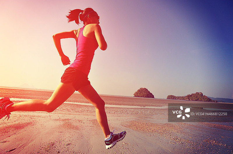 年轻的健身女性在日出的海滩上跑步图片素材