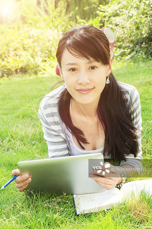 亚洲女学生在校园草地上使用数字平板电脑图片素材