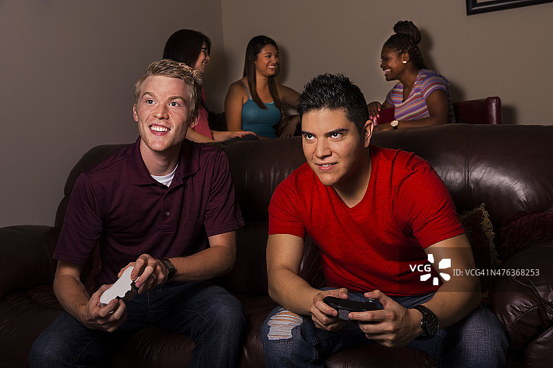 游戏:两个男人玩电子游戏。年轻女性的背景。图片素材