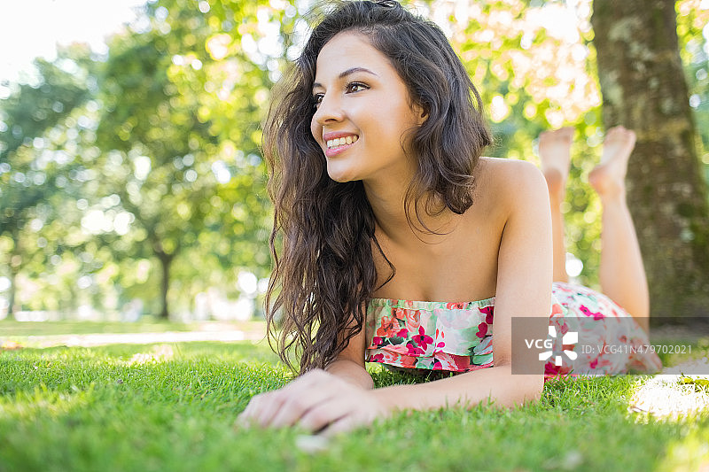 一个漂亮开朗的黑发女人躺在草坪上，看着别处图片素材