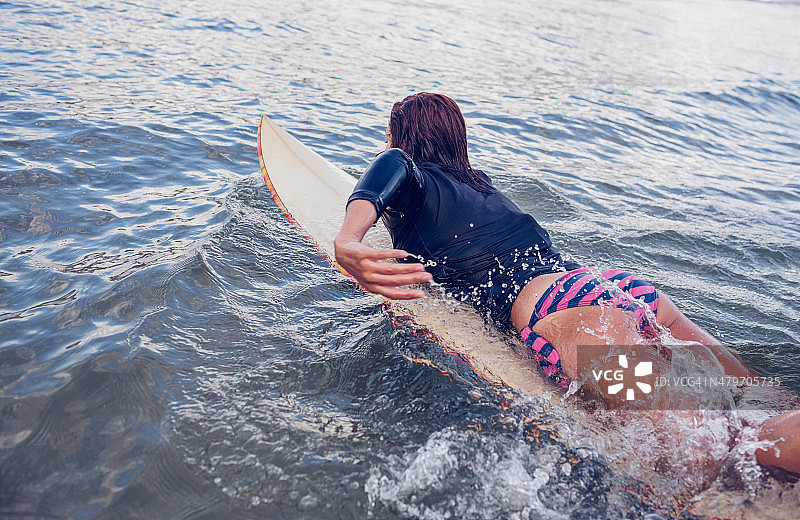 一个女人在水中冲浪板上游泳的后视图图片素材