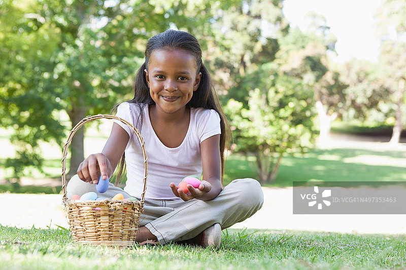 小女孩坐在草地上数着复活节彩蛋，对着镜头微笑图片素材