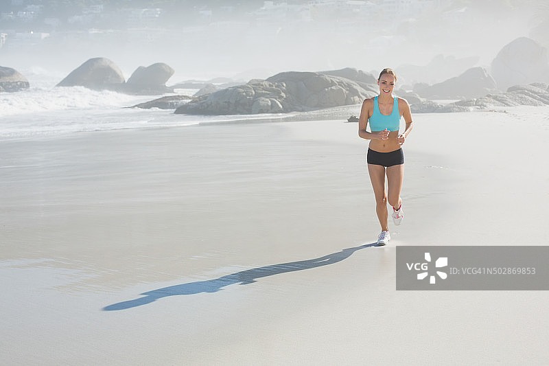 健康的女人微笑着在海滩上慢跑图片素材